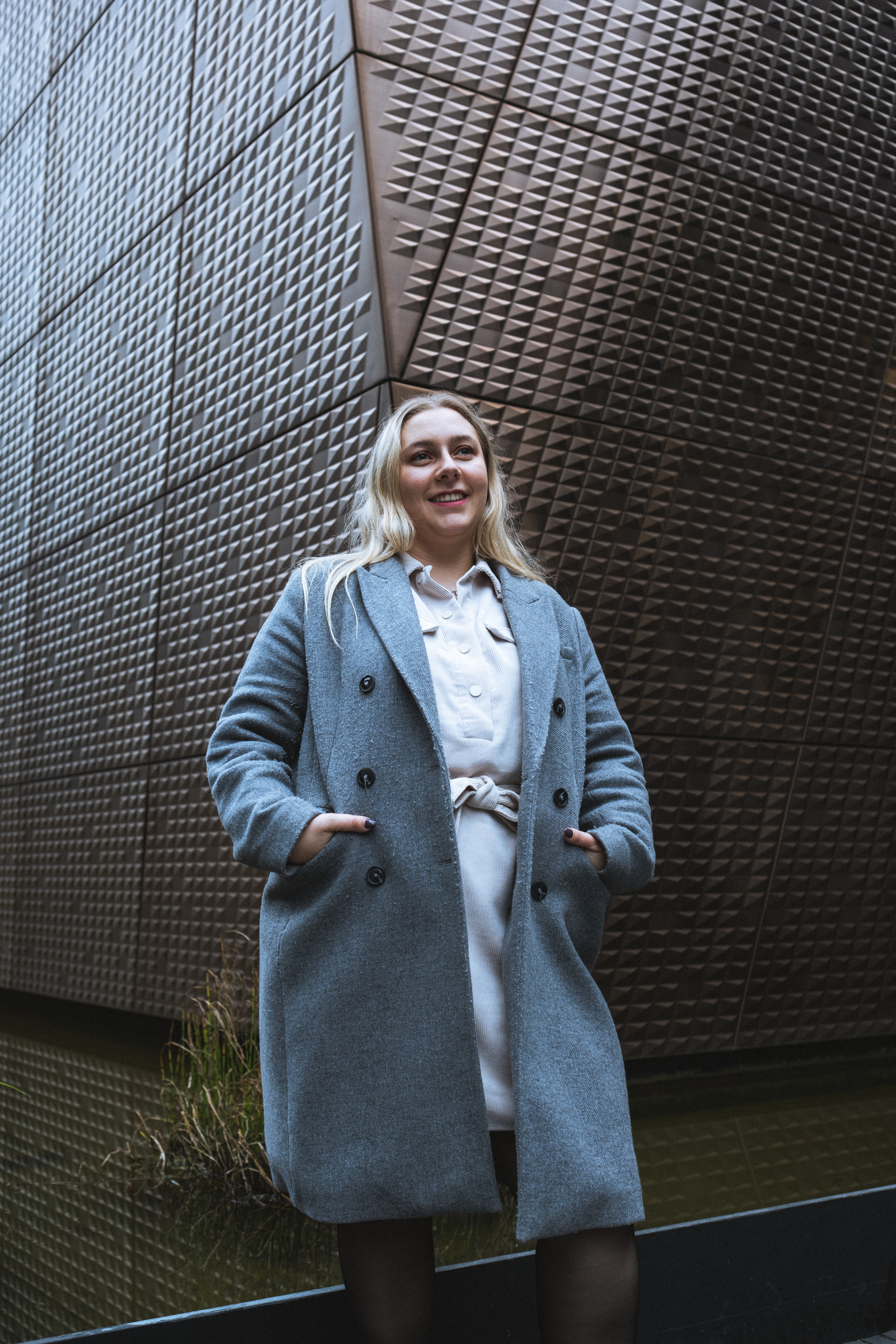 Portrait urbain d’une jeune femme blonde en look casual, prise devant une structure architecturale moderne à Luxembourg